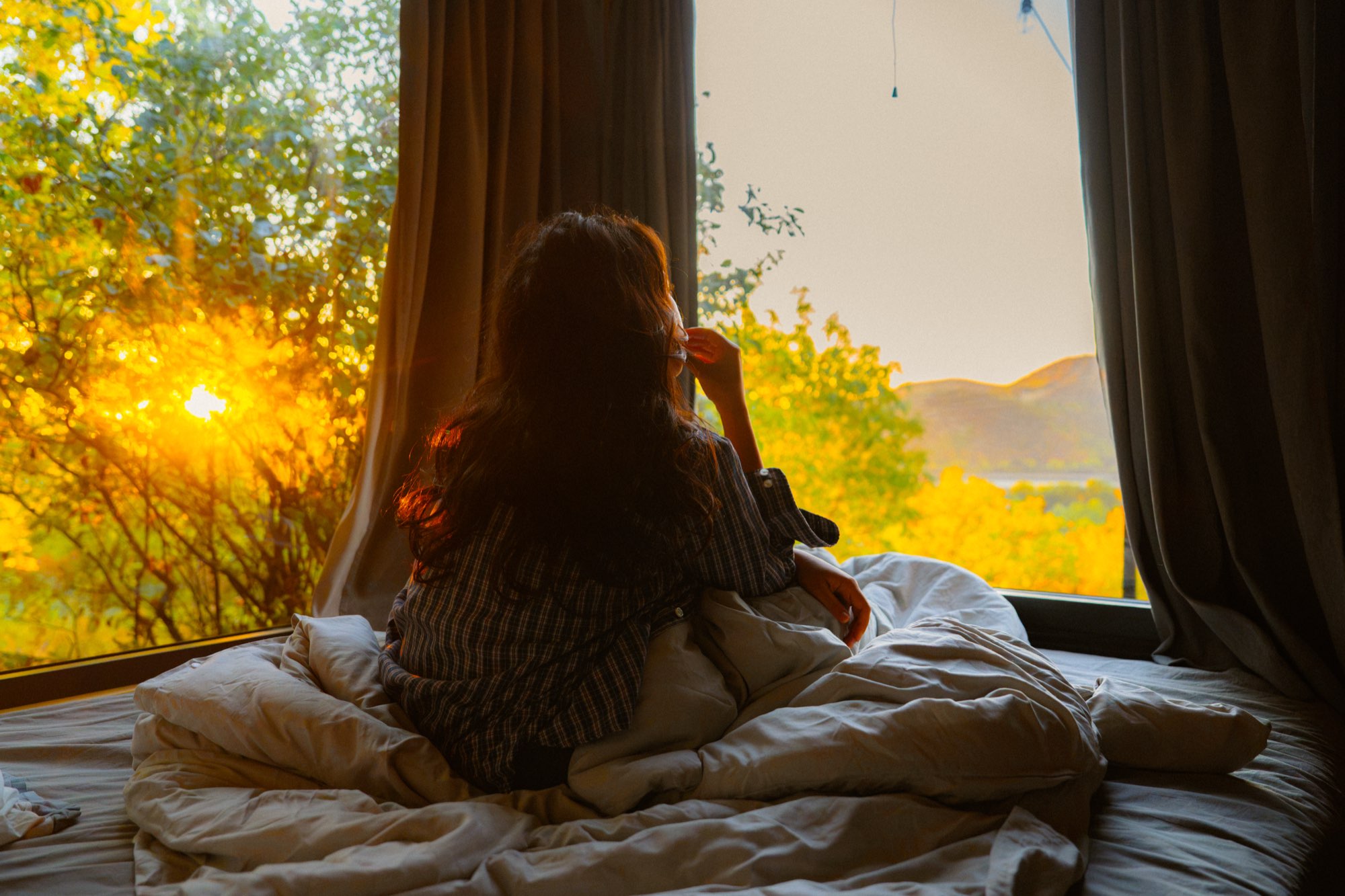 Guest sitting up in bed watching the sunrise through the window