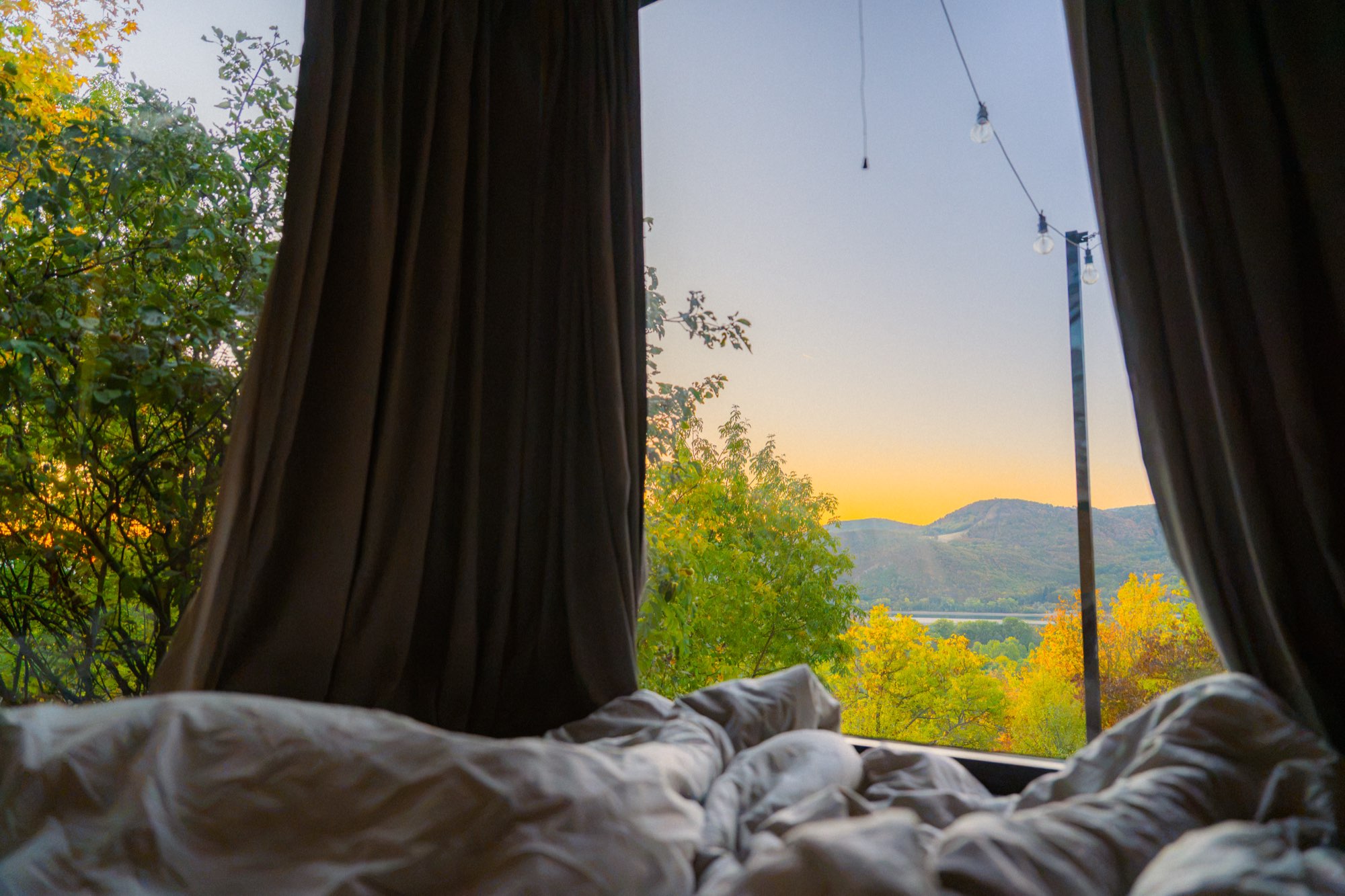 View from the bed through the window to string lights and a sunset sky