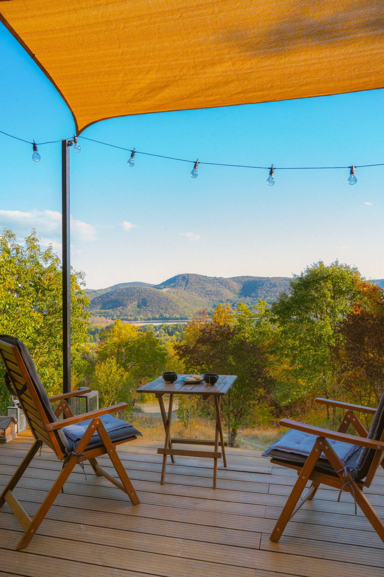 Deck chairs and table under the orange shade sail looking out to the hills